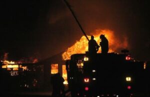 silhouette of firefighters on roof of building with flames